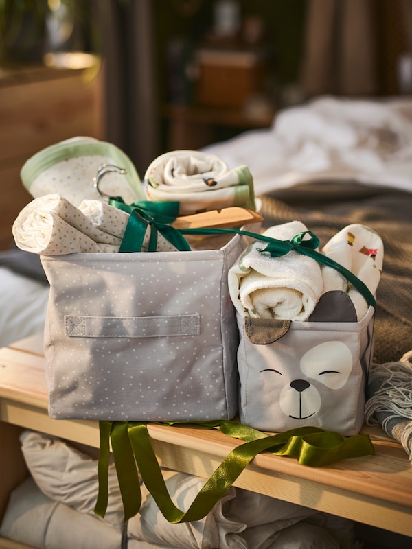 Two gray decorative DRÖMSLOTT boxes with baby textiles in it.