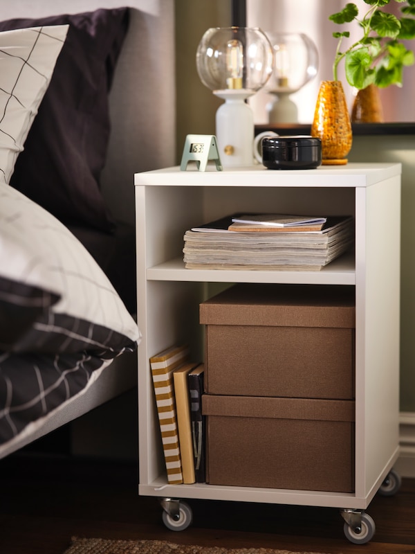 A white VIHALS nightstand on castors next to a bed.