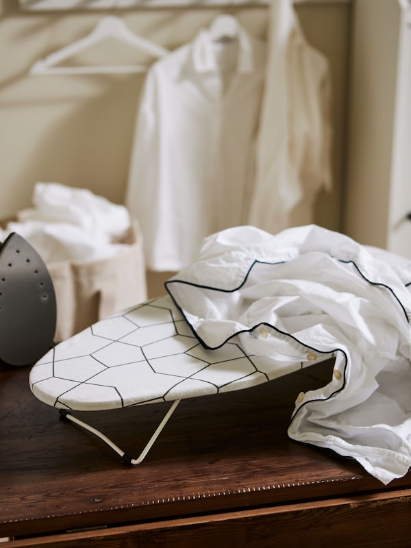 A JÄLL ironing board, table placed on a wooden surface next to an iron and with a white shirt on it.