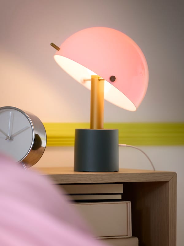 A small side table lamp with a pink round shade slightly tilted and a blue and gold base.