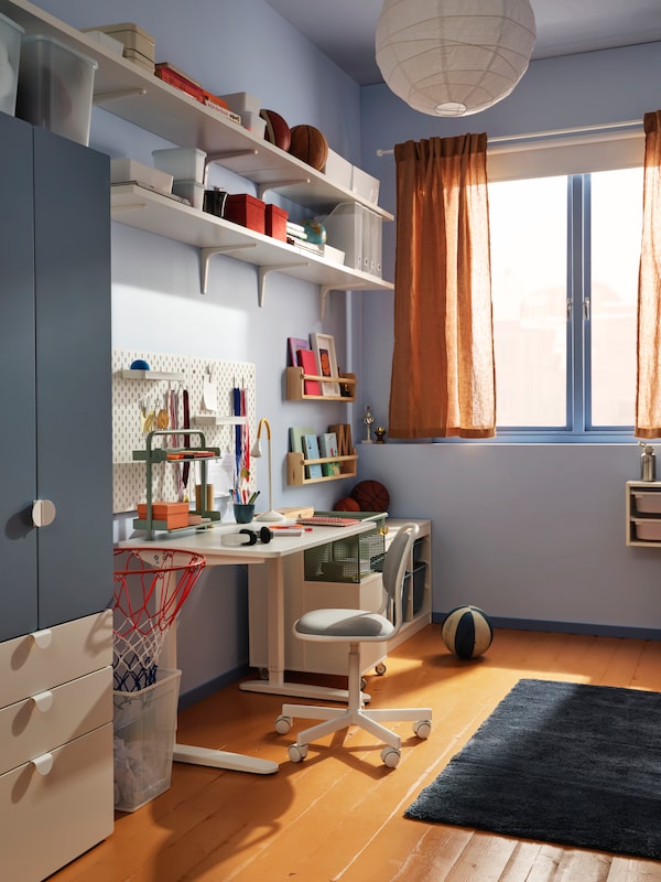 One side of a blue children’s bedroom with high shelves along the wall and a white RELATERA sit/stand desk combination.