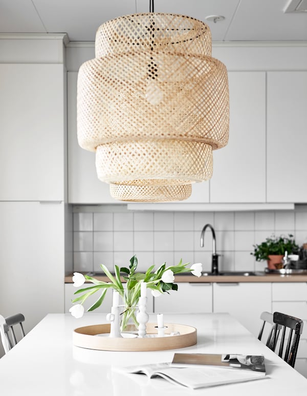 A SINNERLIG pendant lamp hanging over a dining table in a bright white kitchen.