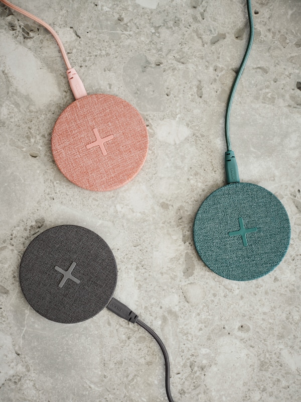 Three wireless chargers sitting on a counter, they're pink, blue and black