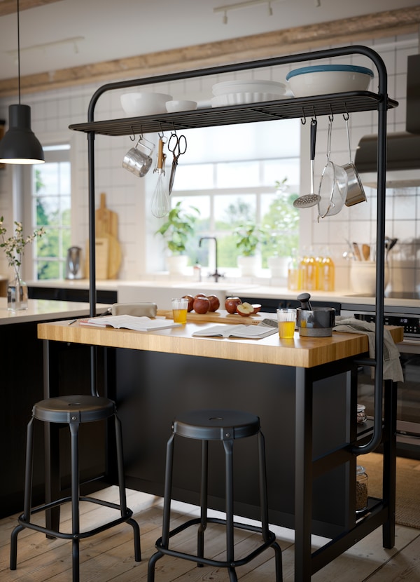 A black kitchen island with a rack hanging over it with kitchen accessories hanging on it.