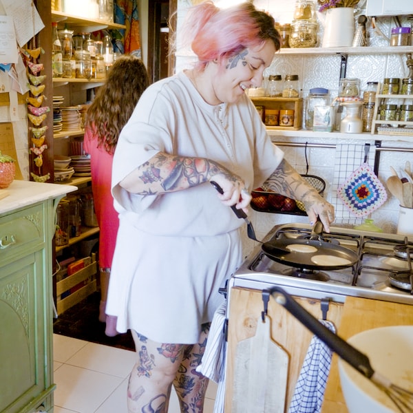 A smiling woman is making pancakes in a HEMLAGAD pancake pan on the stove.