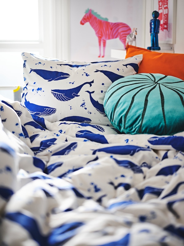 A kids bed with a duvet covered in whales and a blue accent pillow on the bed