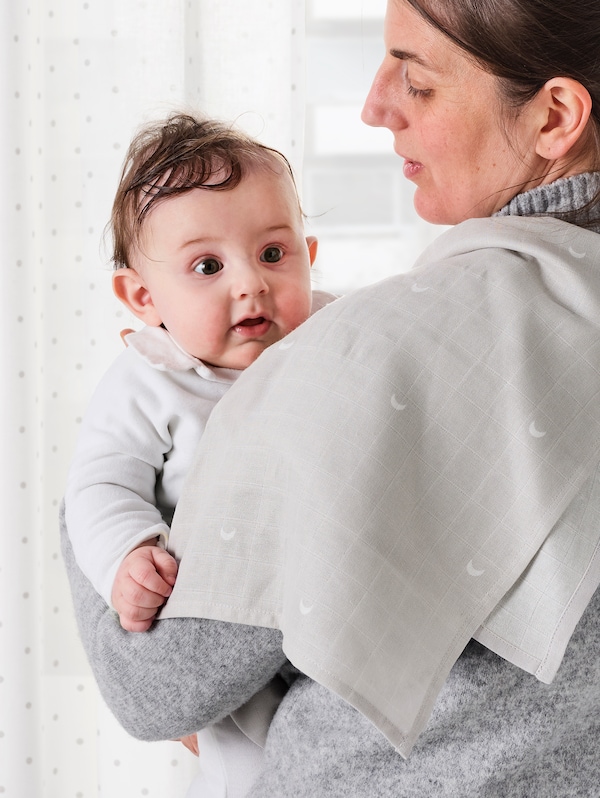 A mother holding a baby with a LEN burp cloth draped over her shoulder.