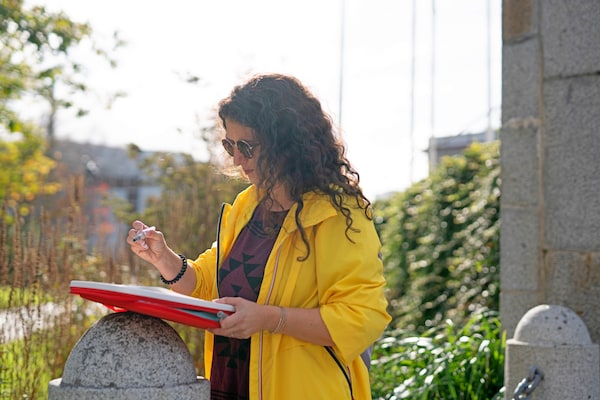 Woman in a yellow raincoat using a MÅLA portable case to draw a painting while out in the city.