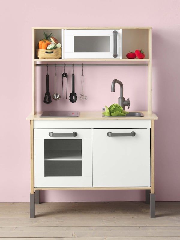 A DUKTIG play kitchen sitting against a pink wall.