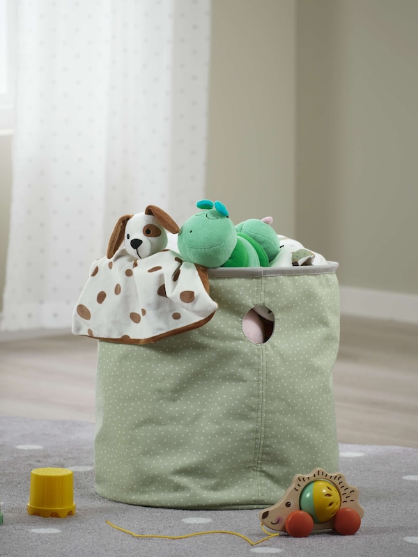 A green storage basket overflowing with soft toys and blankets