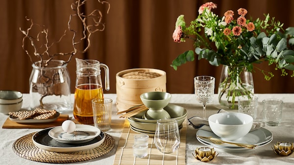 A table displaying three different table settings, including various dinnerware, glassware, place mats and flowers in vases.