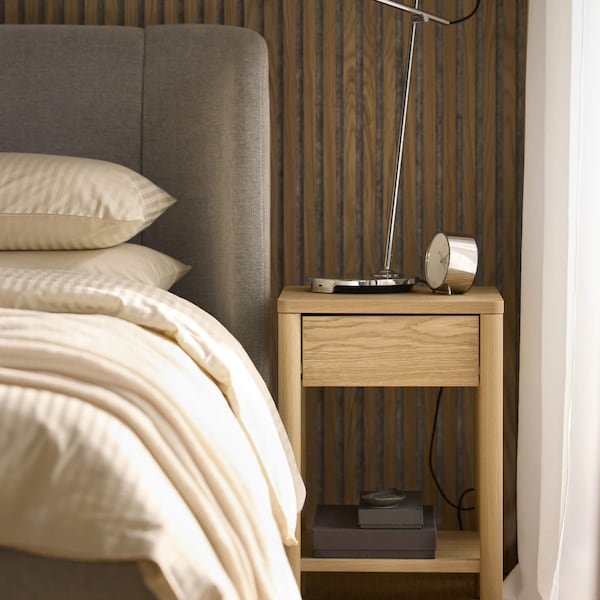 A wooden nightstand next to a bed.