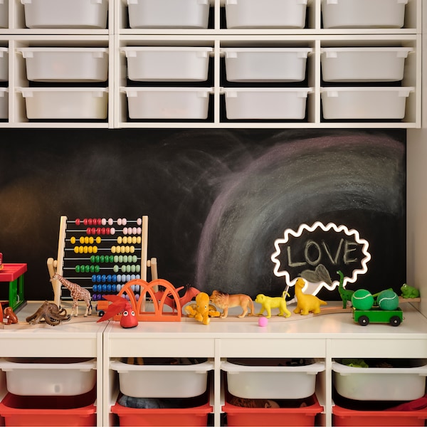 TROFAST storage combinations with boxes stand against a black wall with some wall-mounted TROFAST wall storage above them.