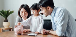 A young child with her parents putting coins into a piggy bank for savings