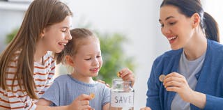 A woman and two children putting coins into a savings jar