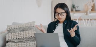 A woman looking at her laptop with her hands up like she is confused