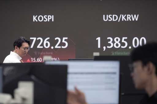 Currency traders watch monitors near a screen showing U