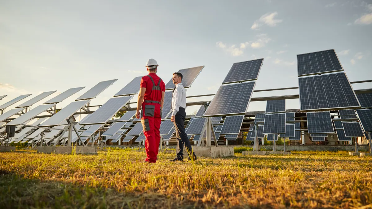 Business executive seen talking to an engineer in workwear in front of solar panels.