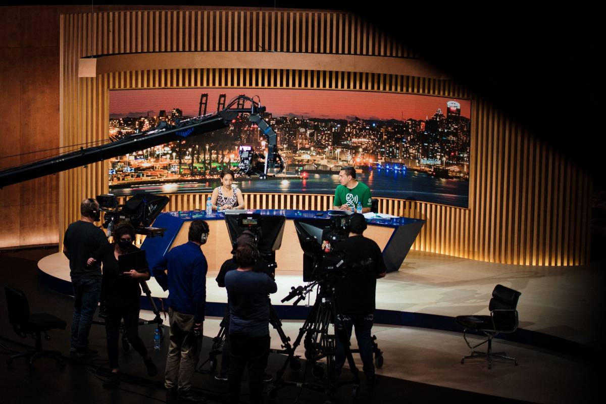 Wide shot of a news desk set, presenters and camera crew rehearsing for the APEC CEO Summit 2021. 