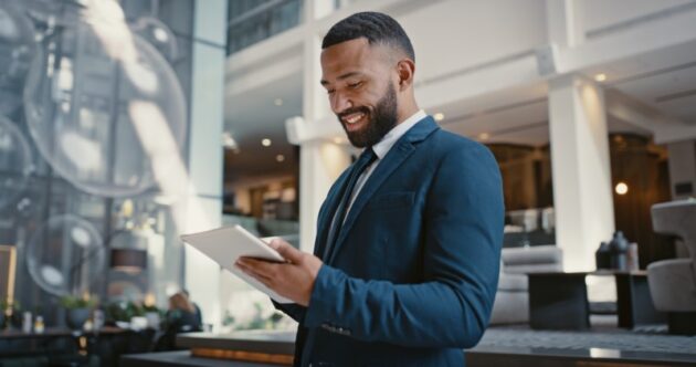 A smiling man standing in a lobby looking at a tablet.