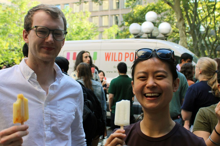 2 students smile and hold up popsicles in a crowd