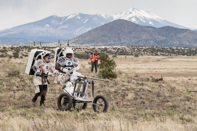 NASA astronauts Kate Rubins and Andre Douglas push a tool cart loaded with lunar tools through the San Francisco Volcanic Field north of Flagstaff, Arizona, as they practice moonwalking operations for Artemis III.
