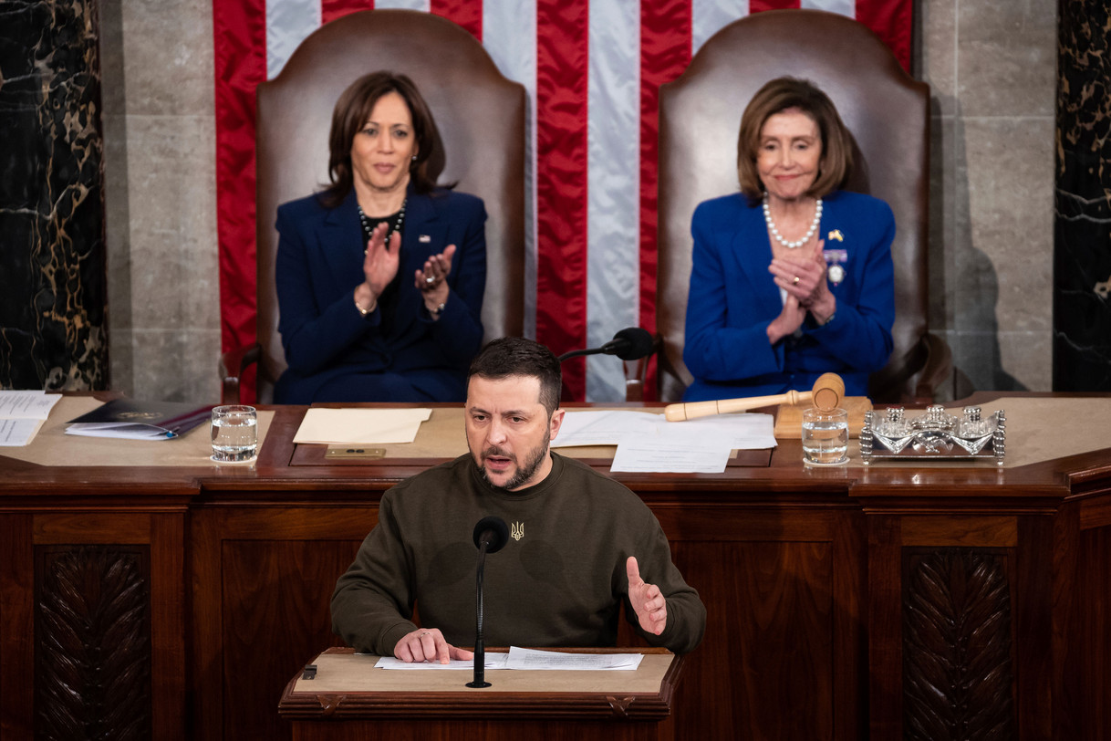Ukraine President Volodymyr Zelenskyy speaking from the dais in the House chamber of the U.S. Capitol, while Vice President Kamala Harris and House Speaker Nancy Pelosi applaud behind him.