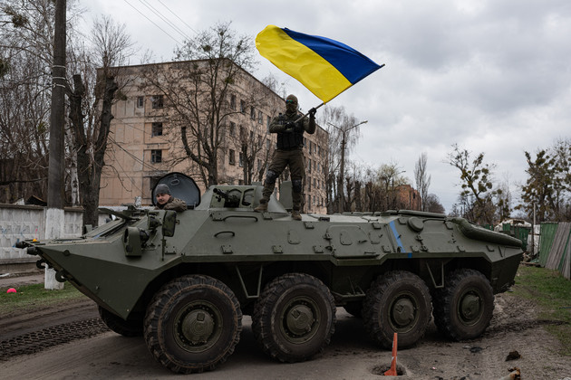 Ukrainian soldier waves Ukrainian national flag while standing on top of an armoured personnel carrier.