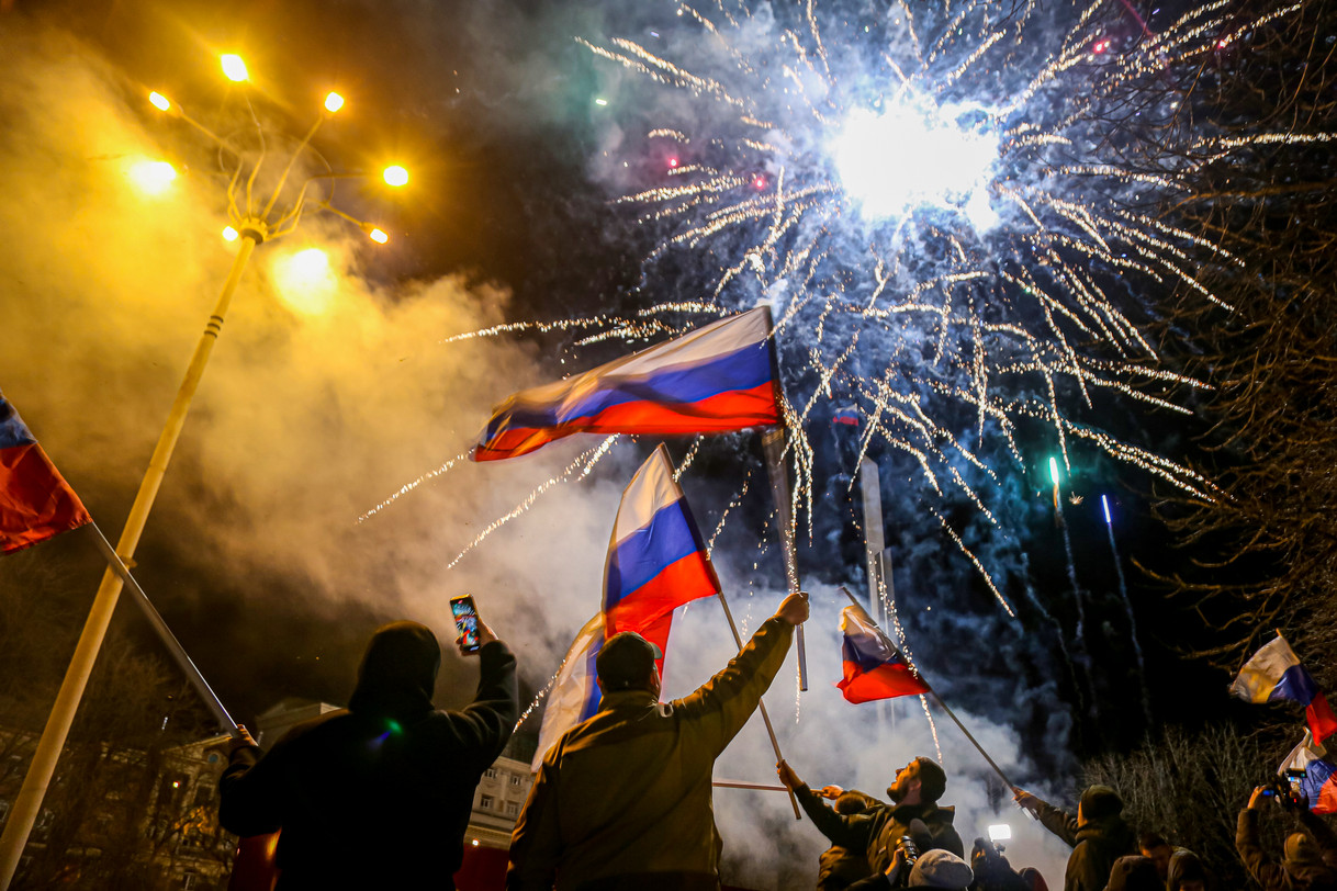 People waving Russian flags as fireworks explode in the night sky.