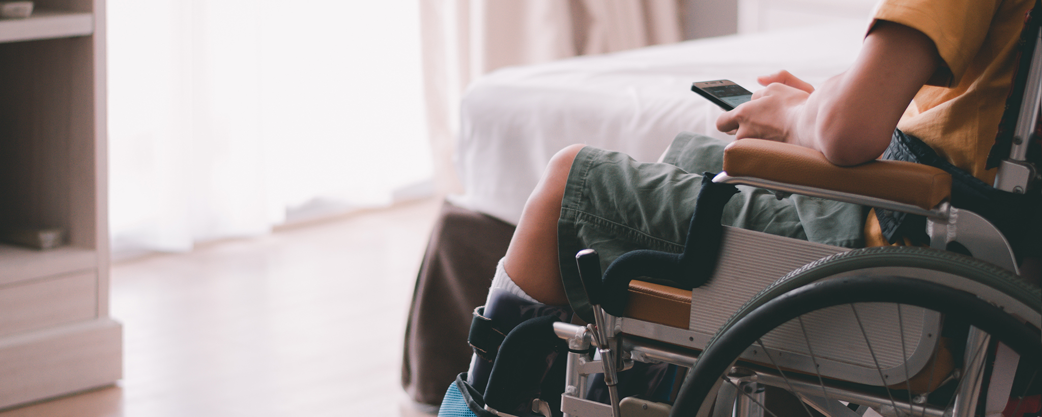 A boy sits in his wheelchair looking at his smart phone. 