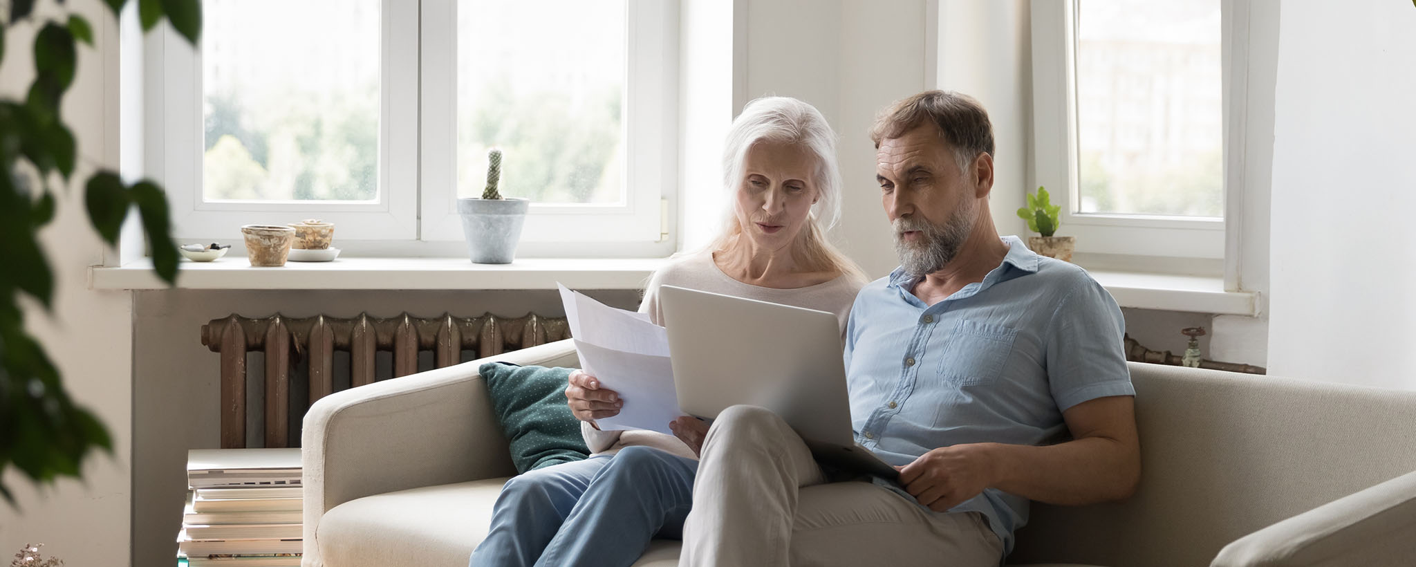 Older adults sitting on a couch looking at a computer, making a plan. 