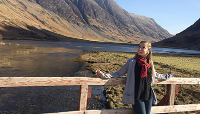 Student standing outside in front of a beautiful river and mountains. 