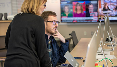 Student sitting in front of computer talking to teacher.