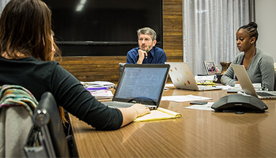 Professor and two students sitting around a large table in the middle of discussion.