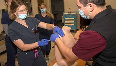 Professor and two students practicing on a nursing mannequin in a simulation lab