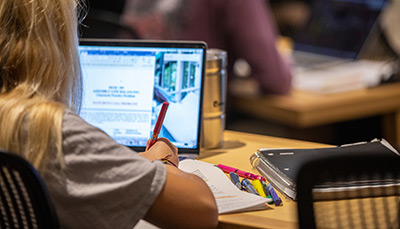 Student sitting in class taking notes with a laptop open.