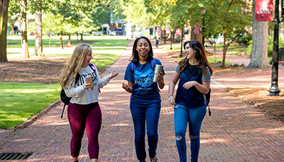 Three students walking down the brick path on the historic horseshoe. 