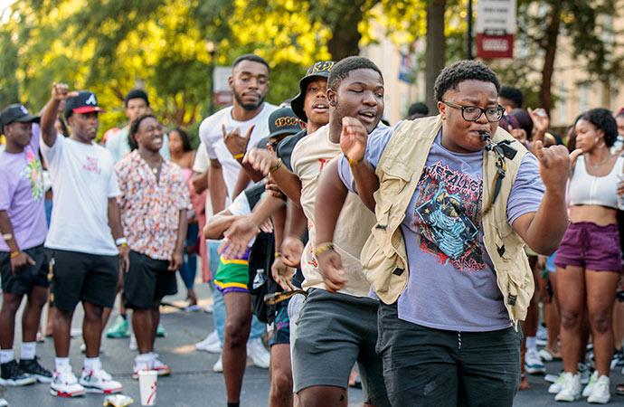 Group of guys dancing in front of a crowd on green street. 