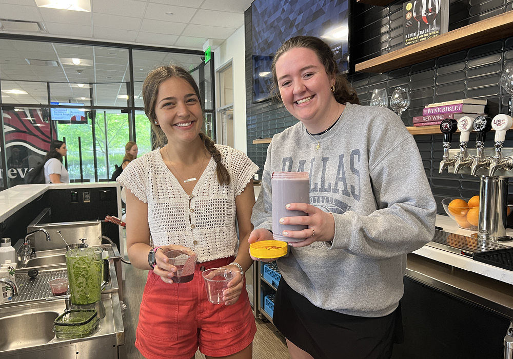 two girls making smoothies in a kitchen and smiling