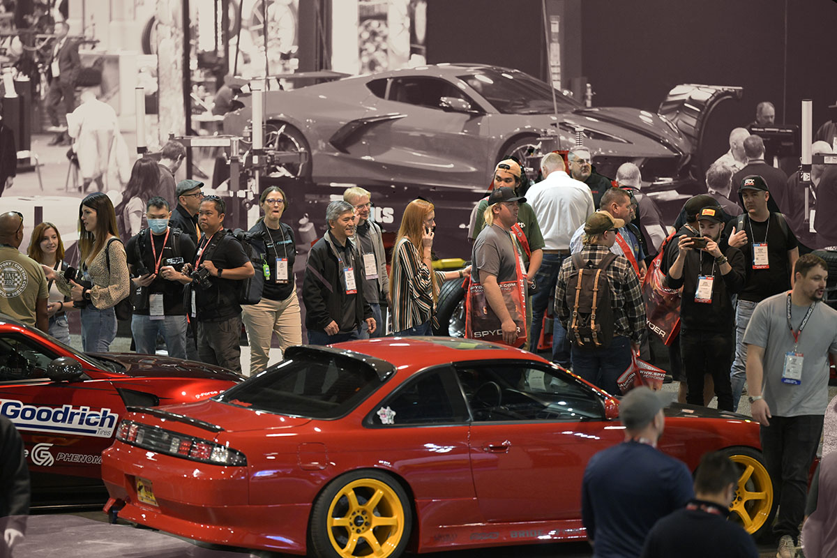 People at the 2024 SEMA SHOW walking past, taking pictures, and observing cars displayed in a booth. 