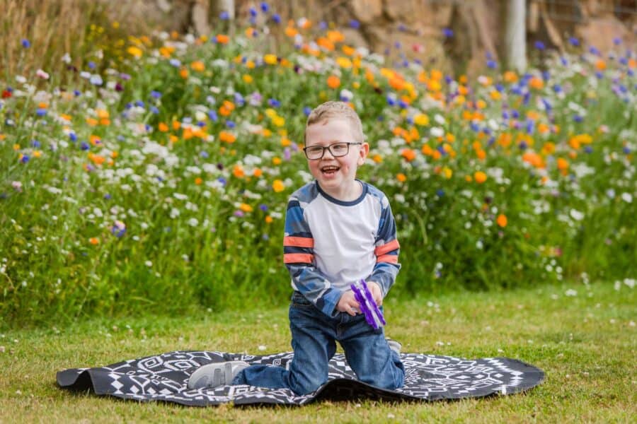 Boy sits on a blanket outside and smiles