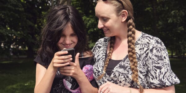 A young girl looks at her phone, smiling with her virtual buddy during an in-person meet up