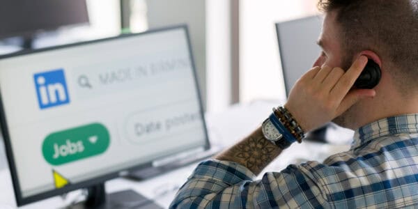 Chris, a white man with short brown hair and tattoos, sitting looking at LinkedIn on a computer monitor.