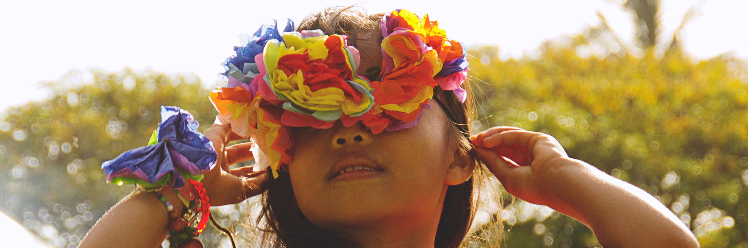 A young girl looks up at the sky and wears fresh flowers on her wrist and head.