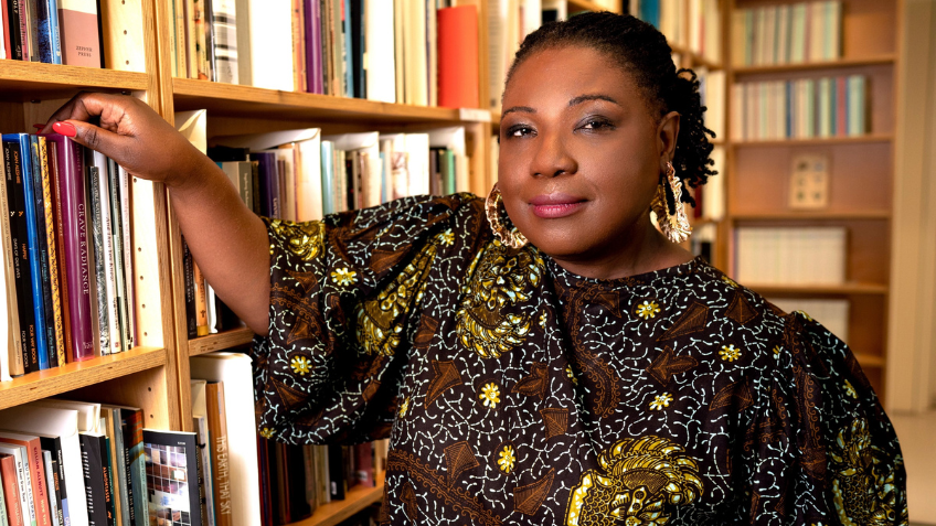 Image of Tracie D Hall standing amongst bookshelves in a library