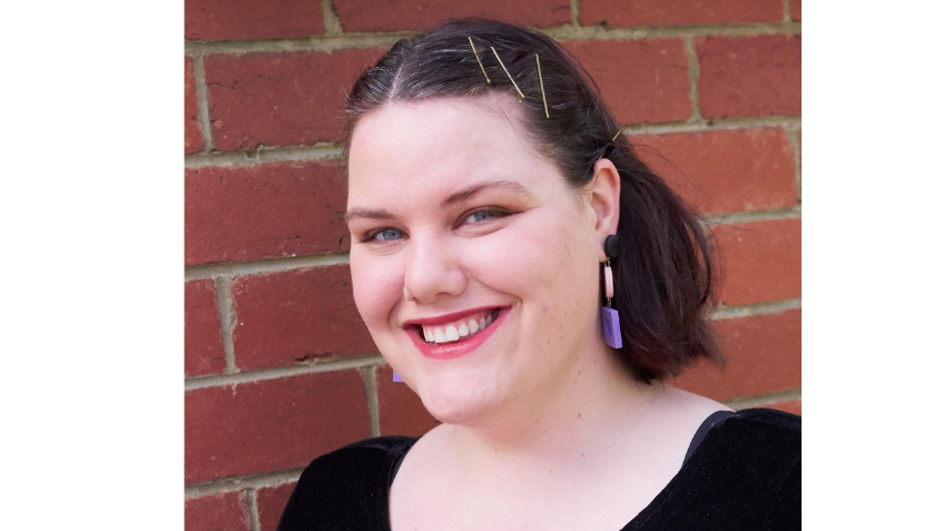 Author Clea Chiller smiling at the camera wearing purple, dangly earring and a black top.