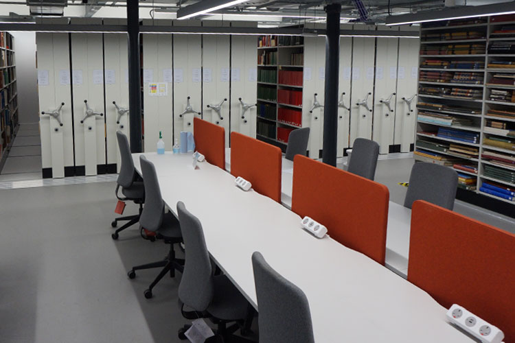 A row of desks and seating is shown in front of shelving.