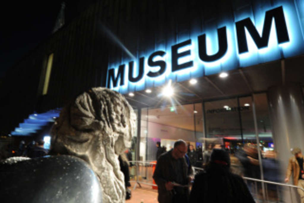 Leuchtender Schriftzug "Museum"  und Menschen vor Museumseingang im Dunkeln, Link auf Kultur