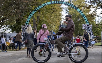 A man carrying a stack of books cycles past an entrance of the Cheltenham Literature Festival