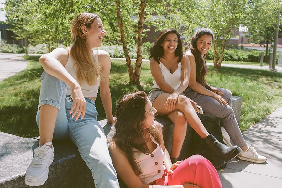 Three students talking on plaza under a tree.